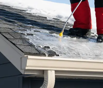 Ice dam removal technician using a steam wand to melt thick ice buildup on a residential roof in Columbus, OH
