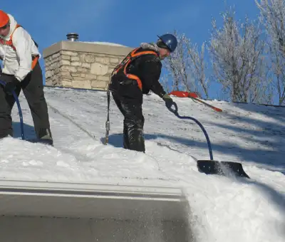 Professional technicians performing roof snow removal with safety harnesses and shovels in Columbus, OH